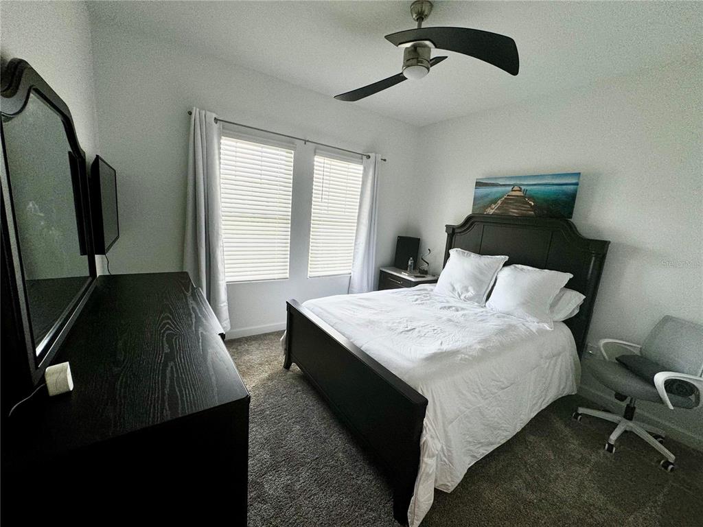 A bedroom features a dark wood bed frame, white bedding, a dresser, and a ceiling fan — 4028 REDBRIDGE LOOP, DAVENPORT, FL