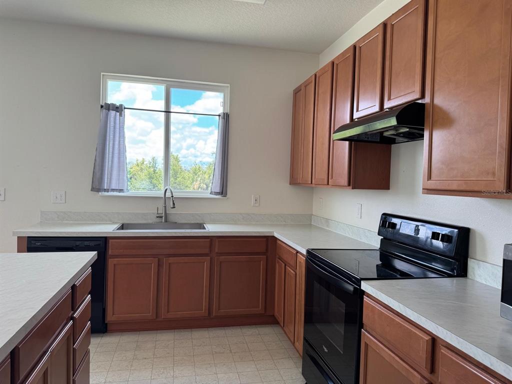 A kitchen features wood cabinets, white countertops, black appliances, and a window above the sink — 709 SARNER PASS WAY, WINTER HAVEN, FL