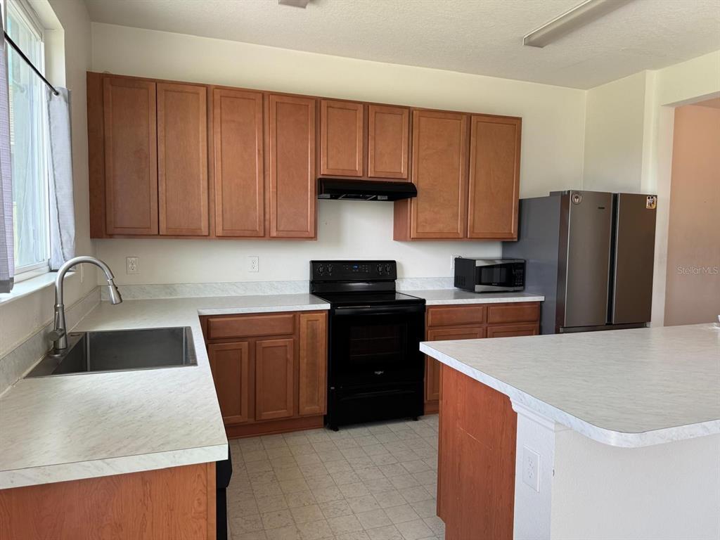 A kitchen features wood cabinets, white countertops, a black stove, and a stainless steel refrigerator — 709 SARNER PASS WAY, WINTER HAVEN, FL