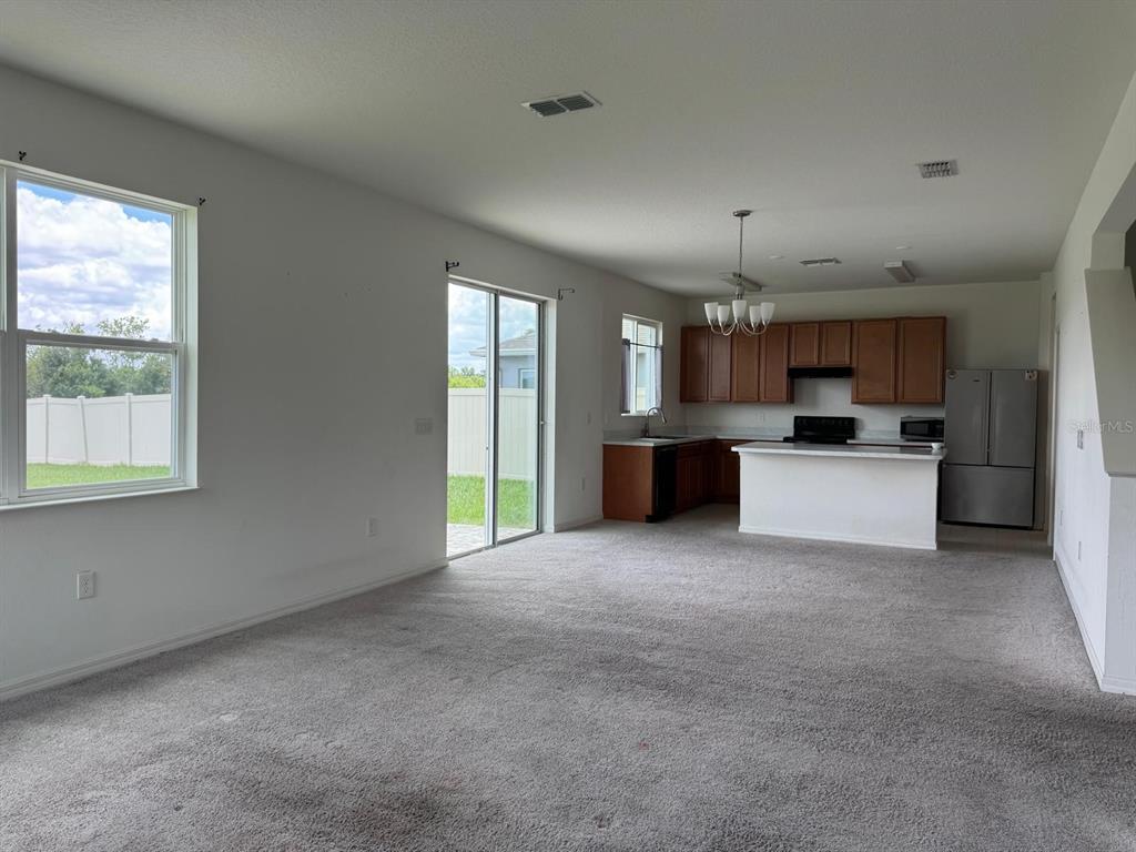 An open-concept living room with gray carpet leads to a kitchen with wood cabinets — 709 SARNER PASS WAY, WINTER HAVEN, FL