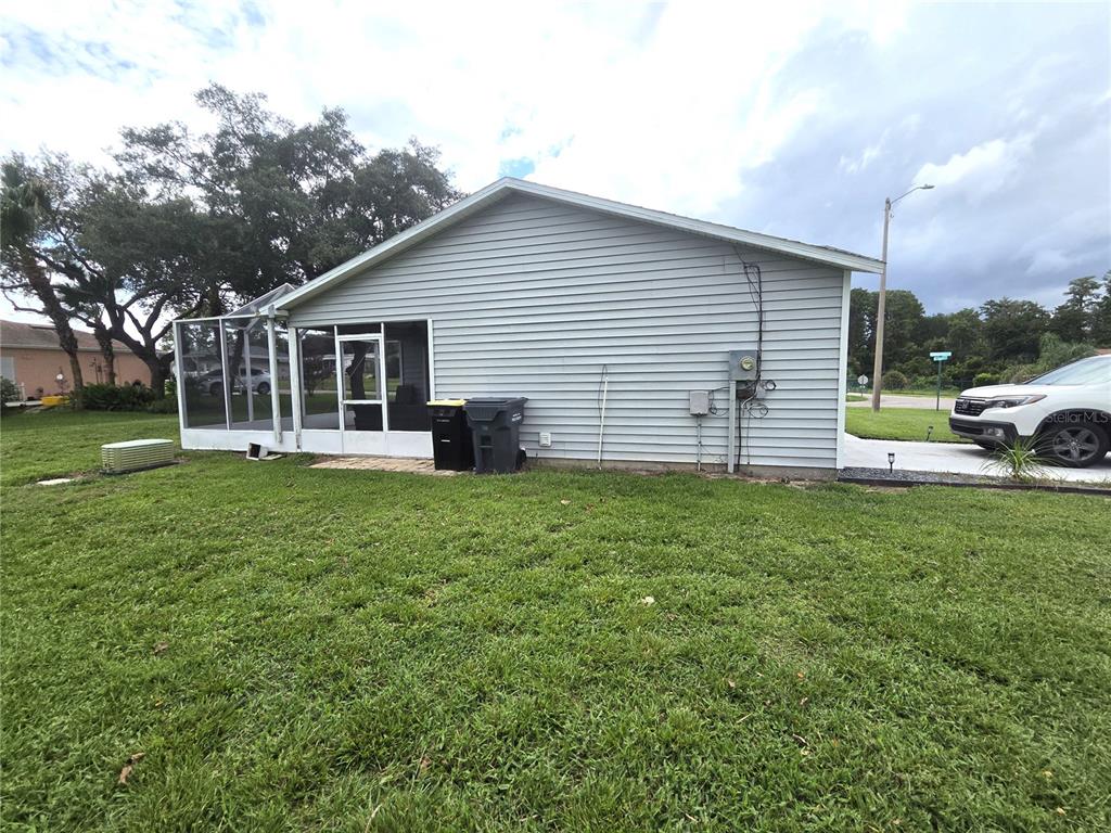 The exterior side view of a house features gray siding, a screened-in porch, and driveway — 7098 ALAMANDA BOULEVARD W, LAKE WALES, FL