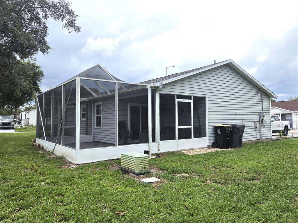A gray-sided house features a large screened-in porch and a green utility box on grass — 7098 ALAMANDA BOULEVARD W, LAKE WALES, FL