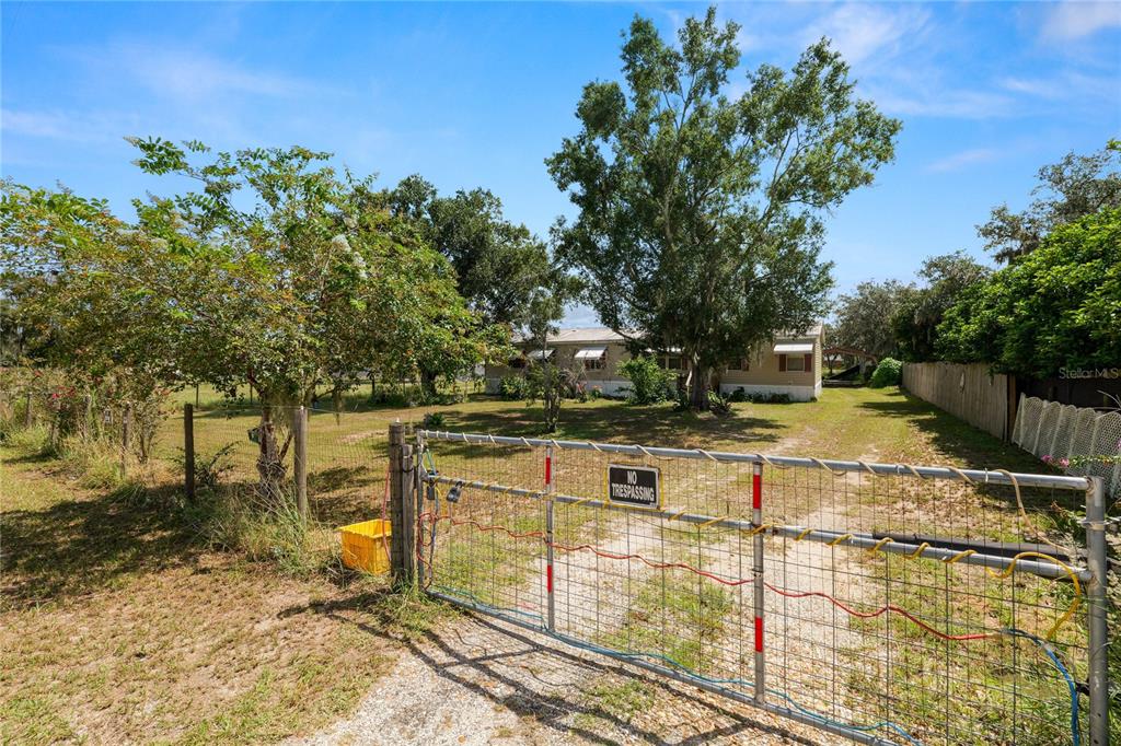 A metal gate secures the entrance to a property with a house and large trees — 1280 OLD STOKES ROAD, FROSTPROOF, FL