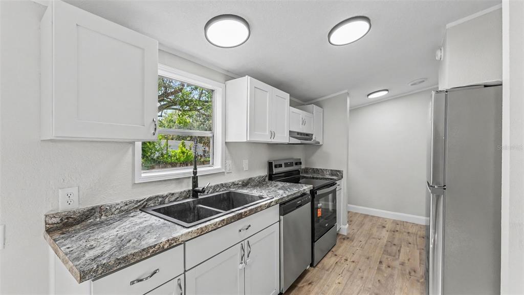 A kitchen features white cabinets, granite countertops, stainless steel appliances, and wood-look flooring — 1222 ROWELL STREET, AUBURNDALE, FL
