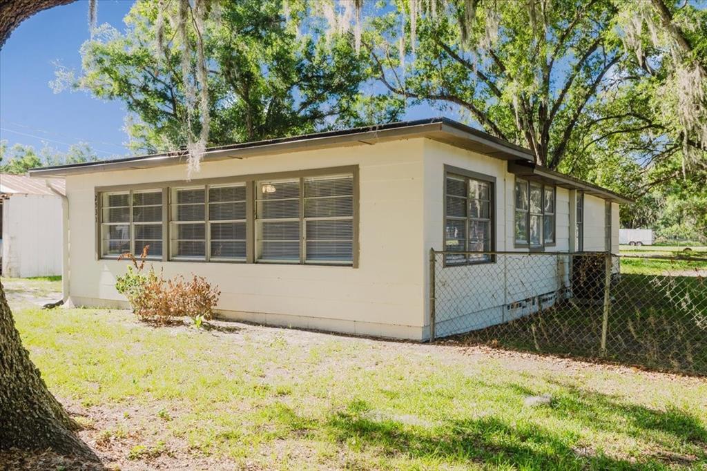 A single-story house with white siding and multiple windows sits behind a chain-link fence — 2531 HEBB ROAD, AUBURNDALE, FL