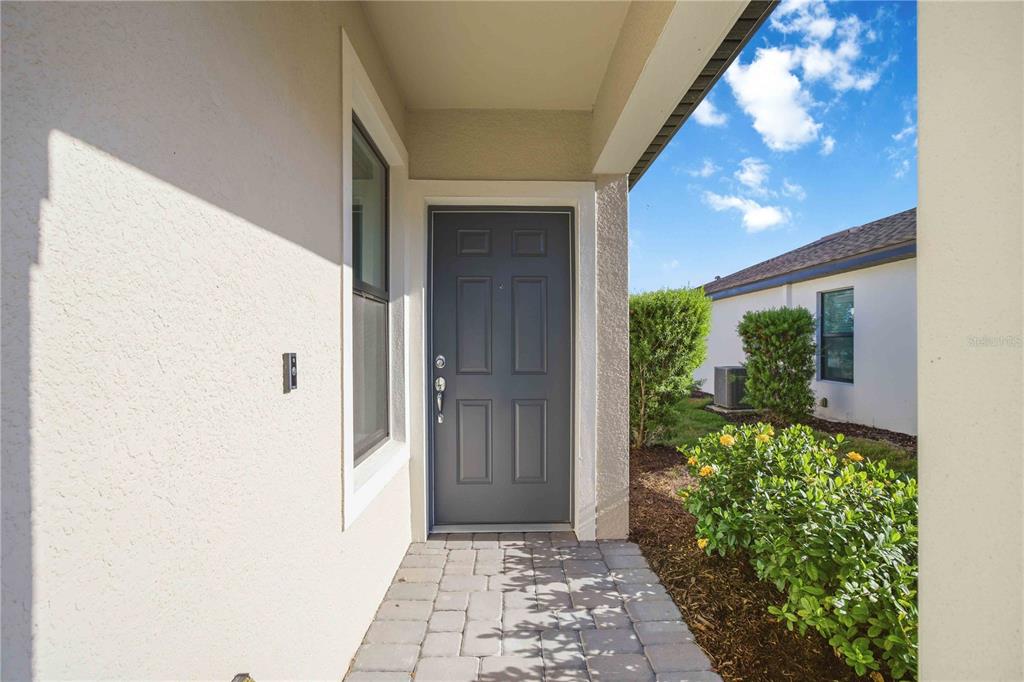A paved walkway leads to a gray front door under a covered entryway — 6548 SILVERSTAR DRIVE, SARASOTA, FL
