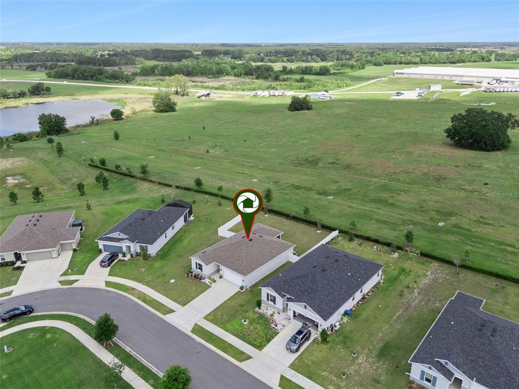 An aerial view shows a suburban house with a fenced backyard bordering an open field — 1682 LITTLELEAF BOXWOOD LOOP, MASCOTTE, FL