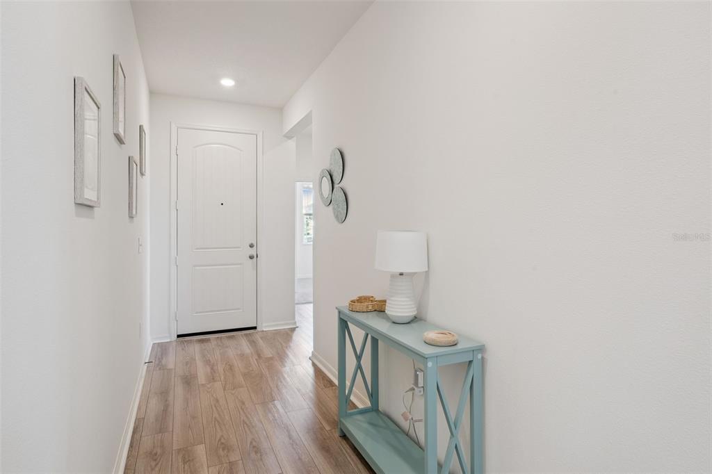 An entryway features wood-look flooring, a light blue console table, and a white front door — 1682 LITTLELEAF BOXWOOD LOOP, MASCOTTE, FL