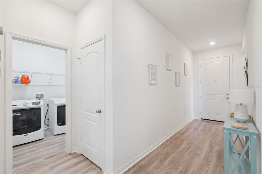 A hallway with light wood flooring leads to a front door and a laundry room — 1682 LITTLELEAF BOXWOOD LOOP, MASCOTTE, FL