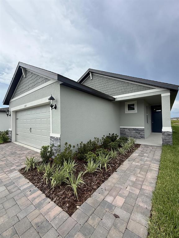 A single-story house with a gray stucco exterior, stone accents, and a paved driveway — 1518 BREKEY WAY, ZEPHYRHILLS, FL