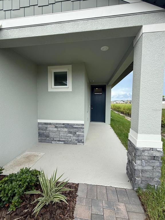 A covered entryway features a dark blue door, stone veneer accents, and a concrete porch — 1518 BREKEY WAY, ZEPHYRHILLS, FL