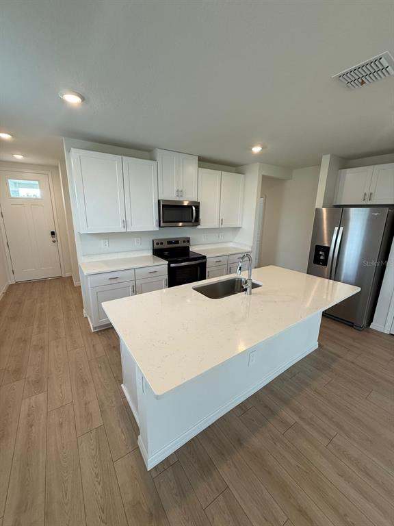 A kitchen features white cabinets, stainless steel appliances, a quartz island, and light wood flooring — 1518 BREKEY WAY, ZEPHYRHILLS, FL