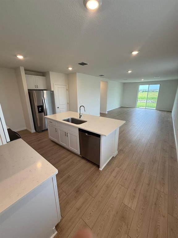 A kitchen with white cabinets, a central island, and light wood-look flooring — 1518 BREKEY WAY, ZEPHYRHILLS, FL