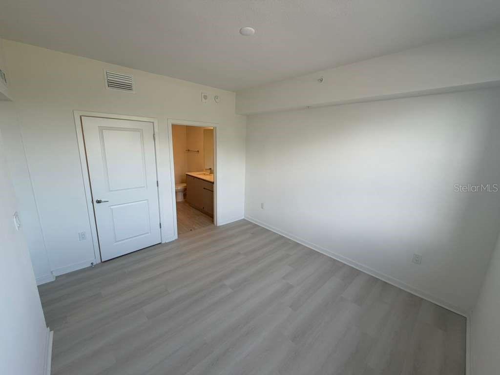 An empty bedroom with light wood-look flooring, white walls, and an attached bathroom — 5587 MILLENIA PARK BOULEVARD UNIT 202, ORLANDO, FL