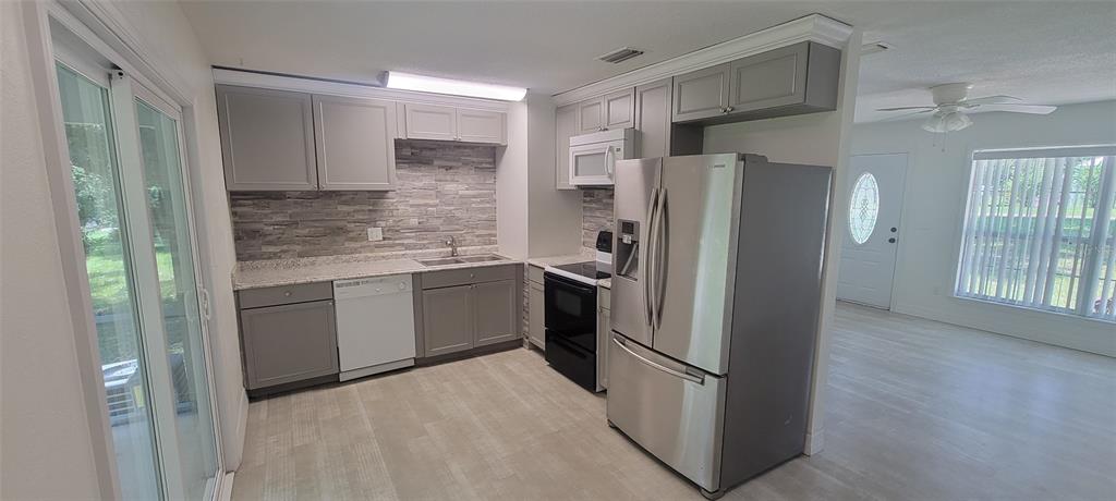 A kitchen area features light wood-look flooring, a white door, and sliding glass patio doors — 1965 MANOR WAY, DELAND, FL