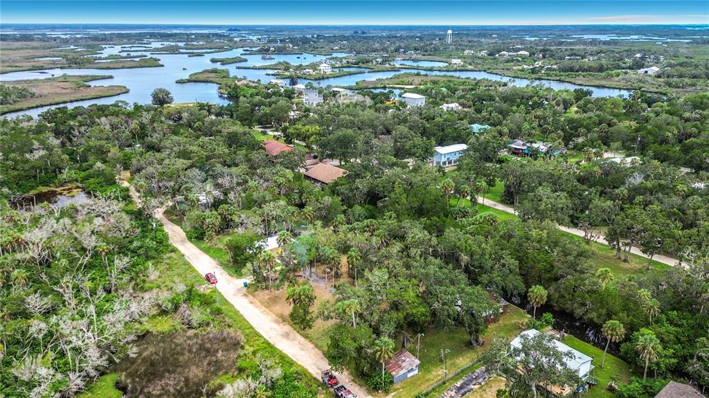 An aerial view shows a dirt road winding through a wooded residential area near water — 14328 W SUTTON COURT, CRYSTAL RIVER, FL