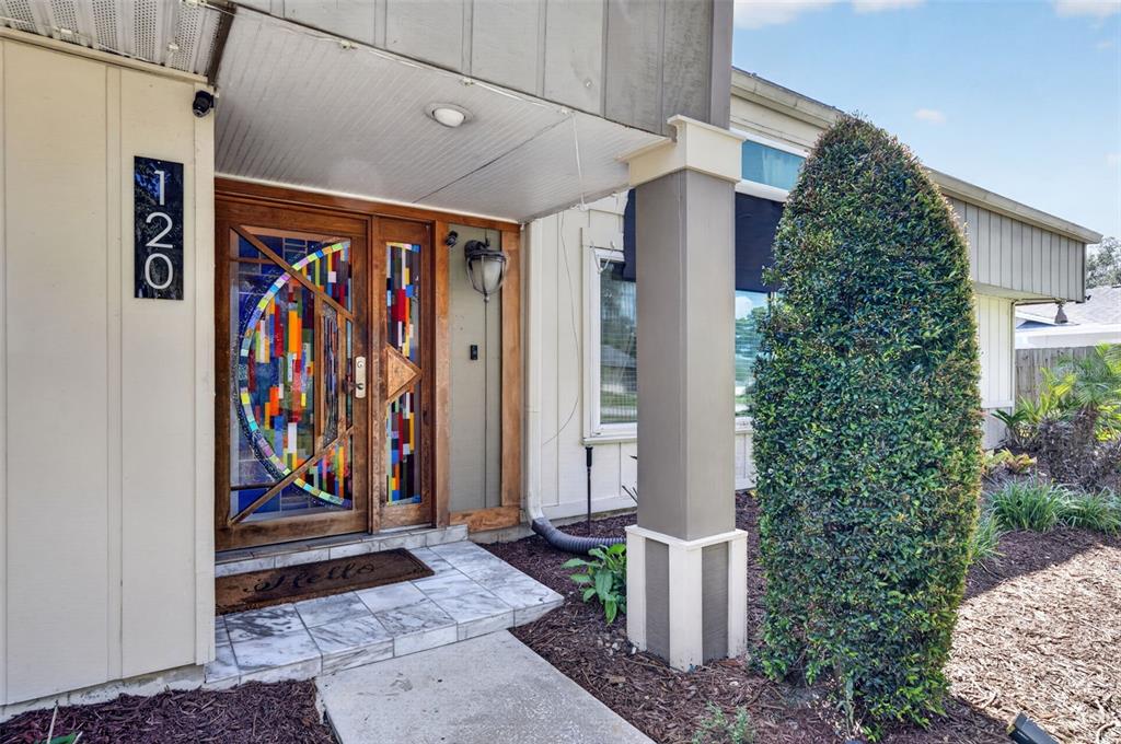 The exterior entrance features a stained glass front door, tiled porch, and a tall shrub — 120 SLADE DRIVE, LONGWOOD, FL
