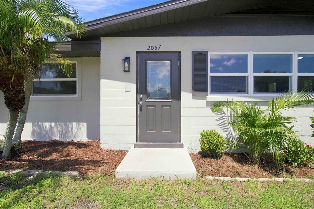 A gray front door with a glass insert is centered on a light-colored exterior wall — 2057 GARDEN PARKWAY, BRADENTON, FL