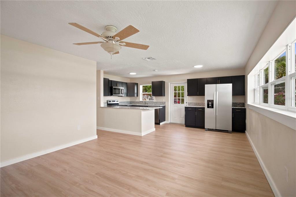 An open-concept kitchen features dark cabinets, granite countertops, stainless steel appliances, and light wood flooring — 2057 GARDEN PARKWAY, BRADENTON, FL