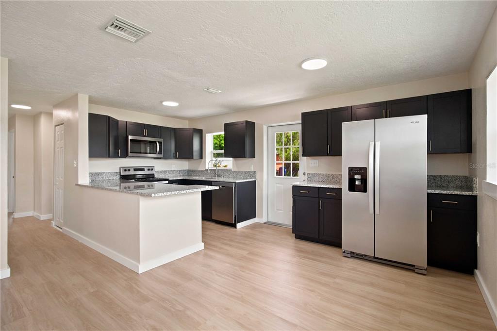 A kitchen features dark cabinets, granite countertops, stainless steel appliances, and light wood-look flooring — 2057 GARDEN PARKWAY, BRADENTON, FL