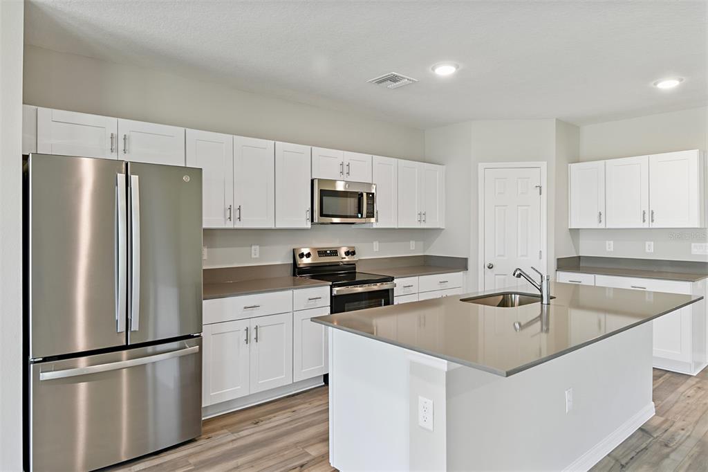 A kitchen features white cabinets, stainless steel appliances, a center island, and gray countertops — 9252 ORCHARD PARK LANE, DADE CITY, FL
