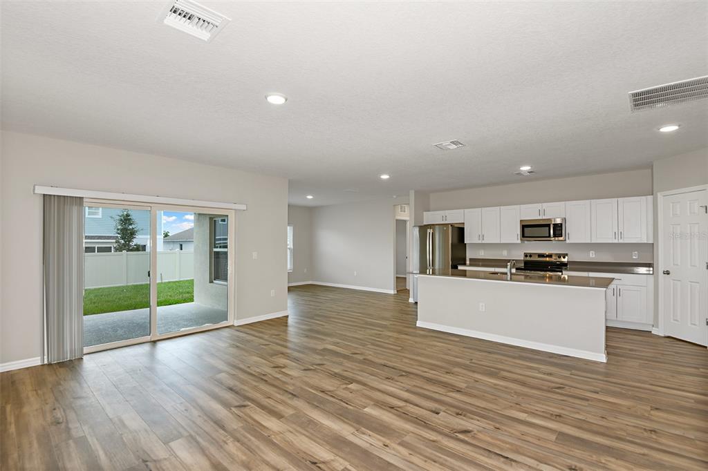 An open-concept kitchen and living area featuring wood-look flooring and a sliding glass door — 9252 ORCHARD PARK LANE, DADE CITY, FL