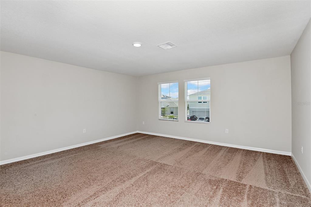 An empty bedroom features beige walls, brown carpet, and two windows with white blinds — 9252 ORCHARD PARK LANE, DADE CITY, FL