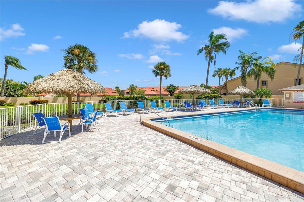 A swimming pool with lounge chairs and tiki umbrellas on a paved patio — 4900 BRITTANY DRIVE S UNIT 205, ST PETERSBURG, FL