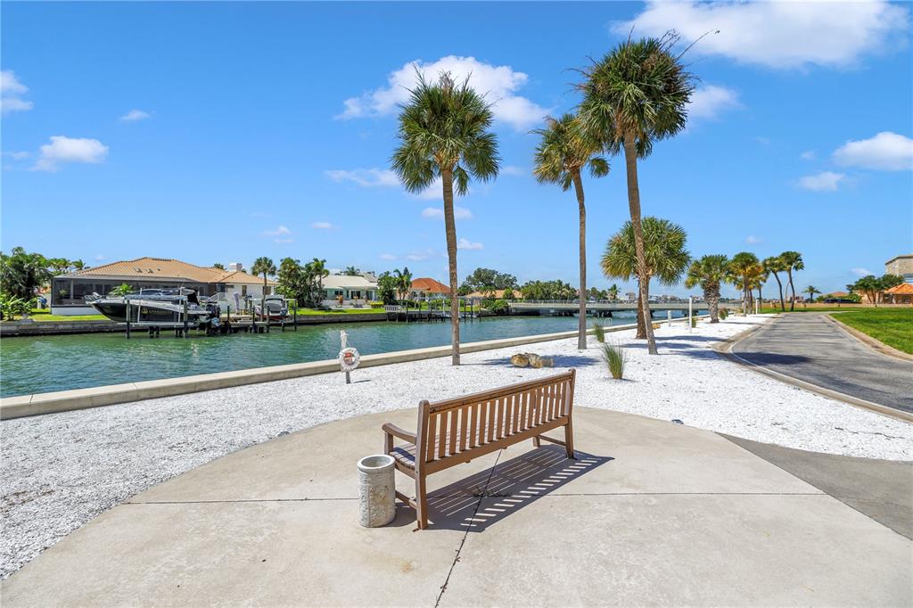 A wooden bench sits on a concrete patio overlooking a canal with palm trees — 4900 BRITTANY DRIVE S UNIT 205, ST PETERSBURG, FL