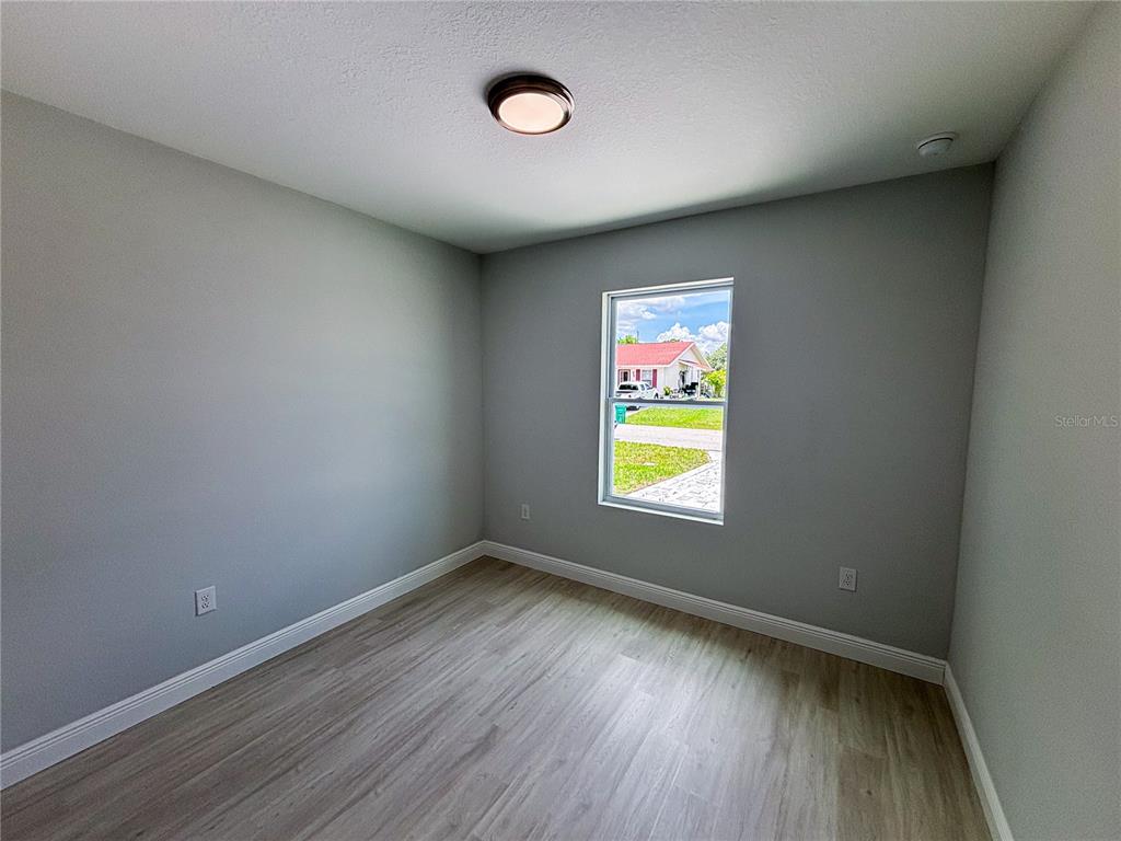 A bedroom with light gray walls, wood-look flooring, a single window, and a ceiling light — 14 TROUT WAY, KISSIMMEE, FL