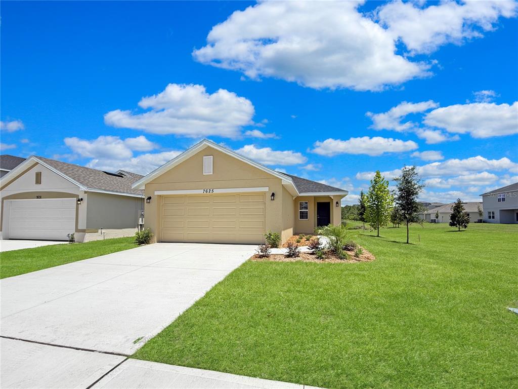 A tan, single-story suburban house features a two-car garage and a concrete driveway — 7625 BENT TREE LOOP, ST CLOUD, FL