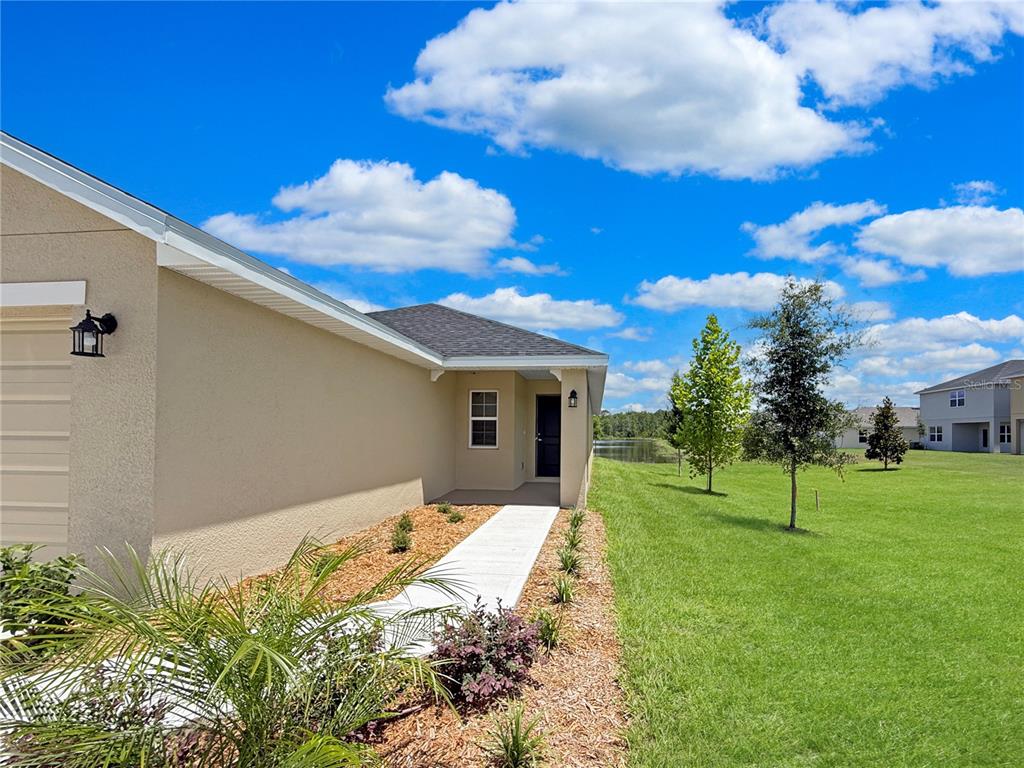 A beige house exterior features a concrete walkway leading to a dark front door — 7625 BENT TREE LOOP, ST CLOUD, FL