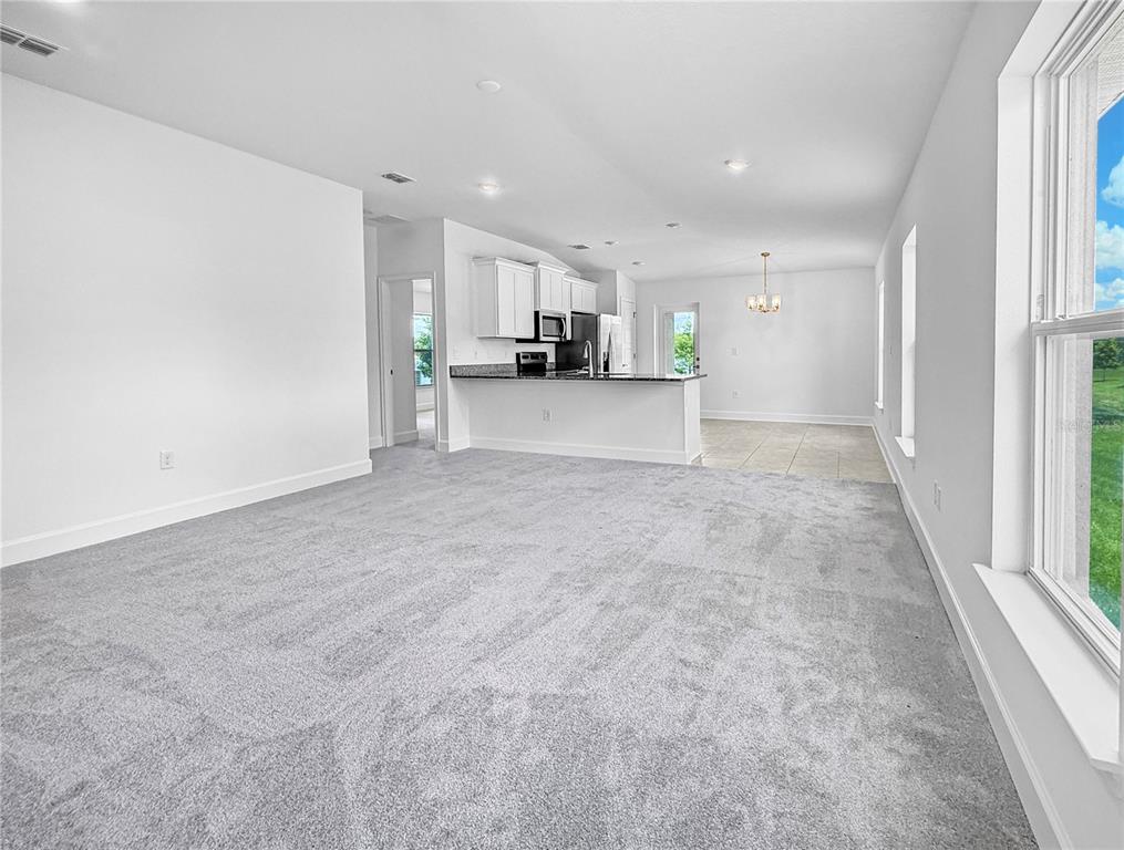 A carpeted living room opens to a kitchen with white cabinets and a dining area — 7625 BENT TREE LOOP, ST CLOUD, FL