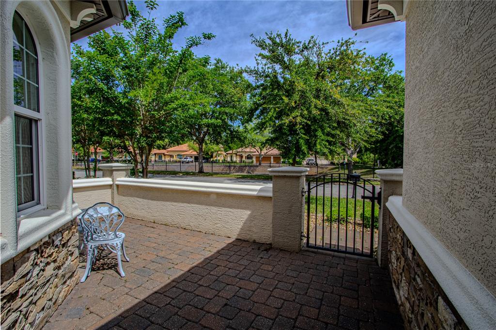 A paved patio features a white metal chair, a low stucco wall, and a gate — 108 VIA ROMA, ORMOND BEACH, FL