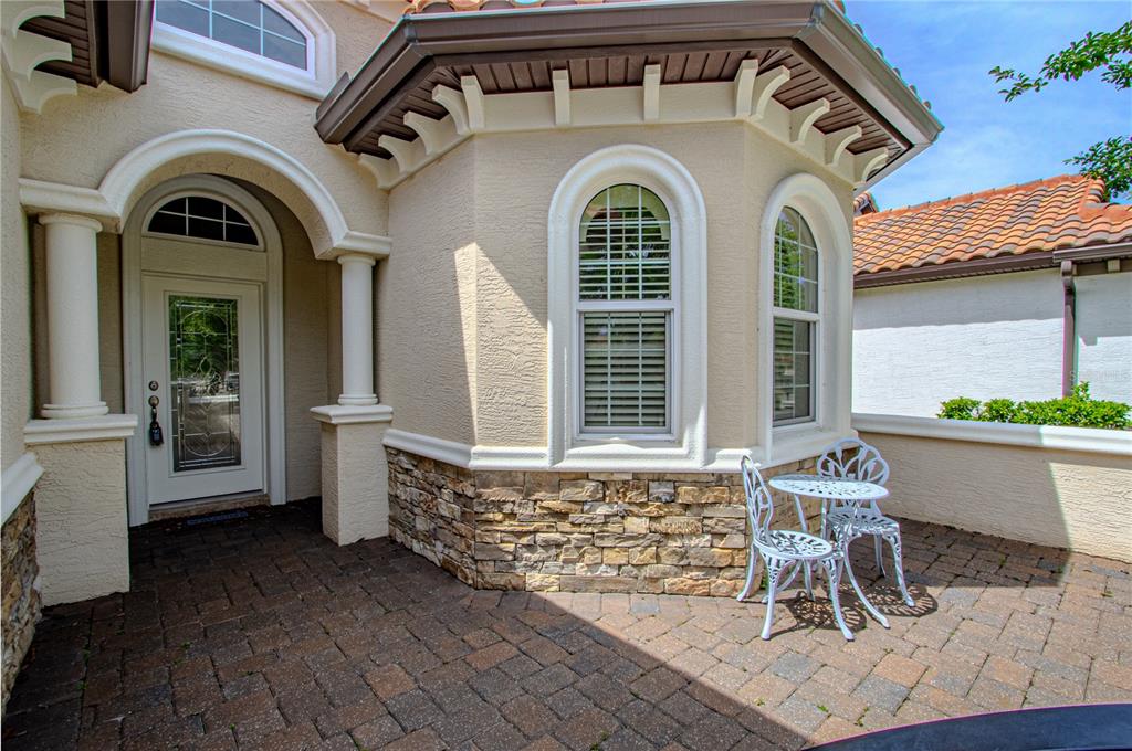 A patio with a bistro set sits in front of a house with stone accents — 108 VIA ROMA, ORMOND BEACH, FL
