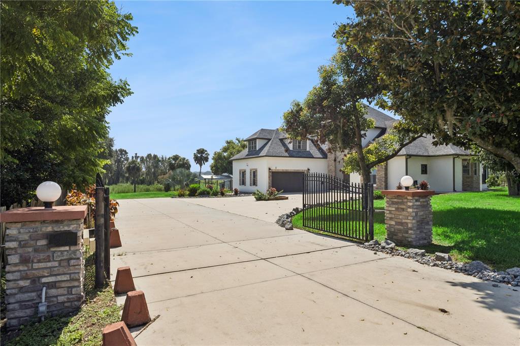A gated concrete driveway leads to a two-story house with a garage and landscaped yard — 91 WOODLAND DRIVE, HAINES CITY, FL