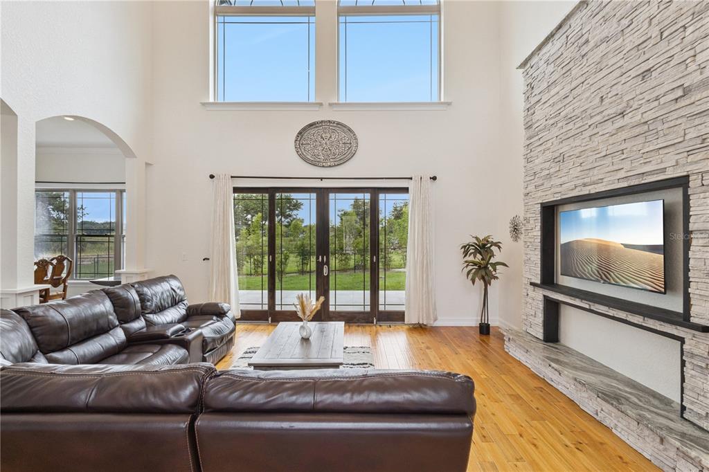 A living room with a stone fireplace, leather sectional, and high windows overlooking a backyard — 91 WOODLAND DRIVE, HAINES CITY, FL