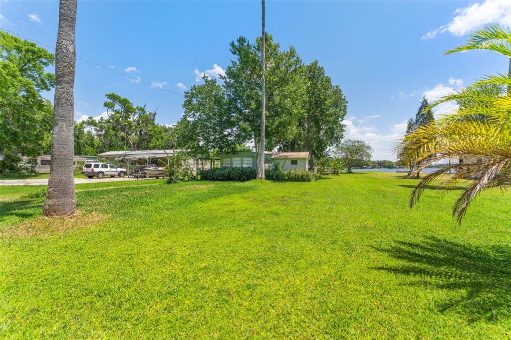 A grassy yard leads to a mobile home with a carport and nearby waterfront view — 7570 BERKLEY ROAD, POLK CITY, FL