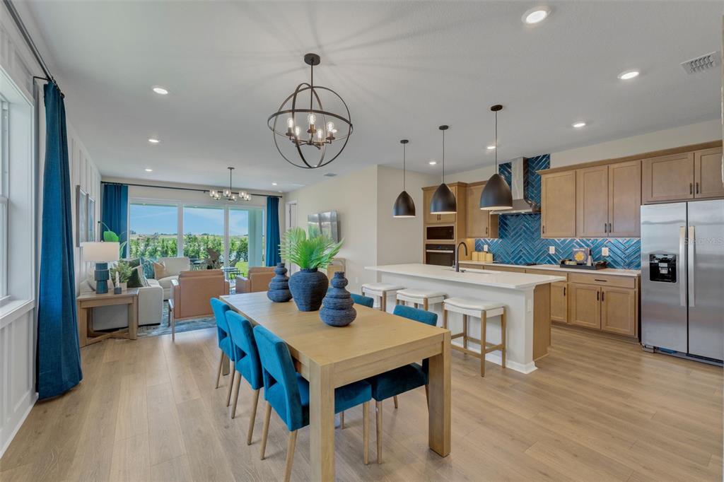 An open-concept kitchen and dining area features light wood floors, blue accents, and pendant lighting — 17078 SQUIRREL BRANCH LANE, ALVA, FL