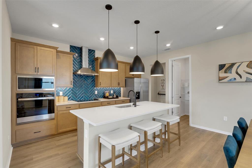 A kitchen features light wood cabinets, a blue herringbone backsplash, and a white island — 17078 SQUIRREL BRANCH LANE, ALVA, FL