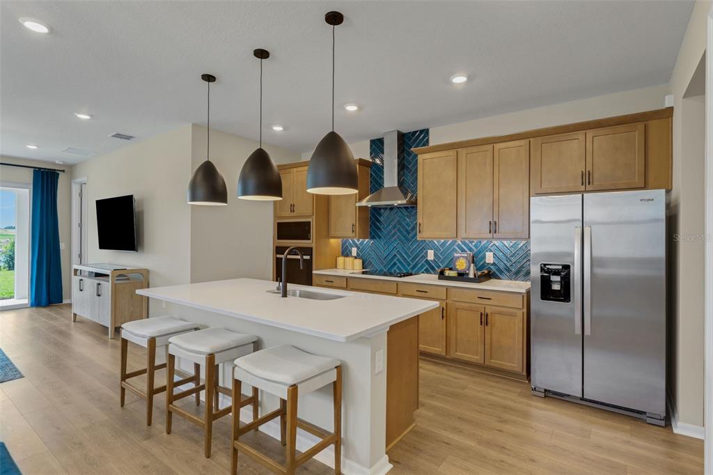 A kitchen features light wood cabinets, a white island with bar stools, and blue backsplash — 17078 SQUIRREL BRANCH LANE, ALVA, FL