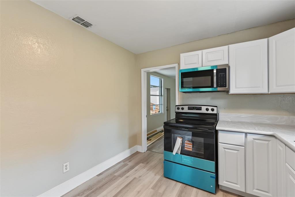 A kitchen features white cabinets, a black stove, a microwave, and light wood-look flooring — 6317 N CENTRAL AVENUE, TAMPA, FL