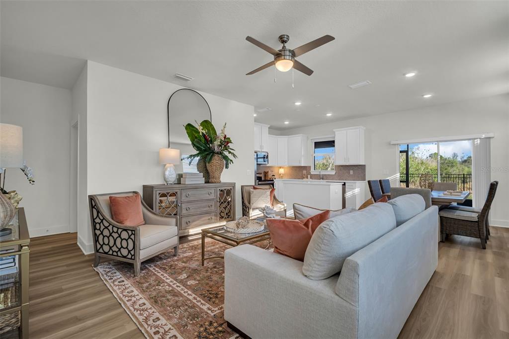A bright open-concept living room features a sofa, armchairs, and a kitchen in the background — 13992 EMERALD FIELDS DRIVE Lot 24, HUDSON, FL