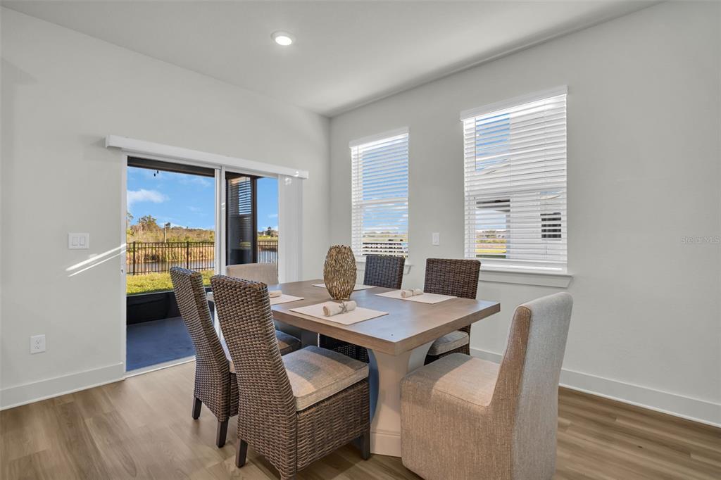 A dining area features a wooden table, wicker chairs, large windows, and a sliding glass door — 13992 EMERALD FIELDS DRIVE Lot 24, HUDSON, FL
