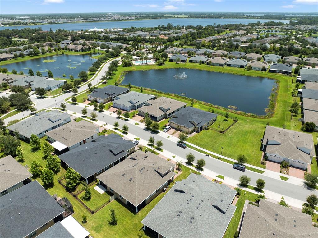An aerial view shows a suburban neighborhood with houses surrounding a pond and fountain — 2516 DATURA LOOP, ST CLOUD, FL