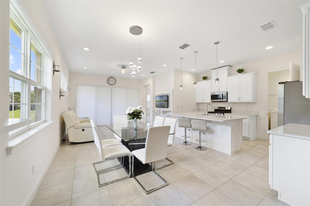 A bright, open-concept kitchen and dining area featuring white cabinetry, a glass-top table, and tile flooring — 2516 DATURA LOOP, ST CLOUD, FL
