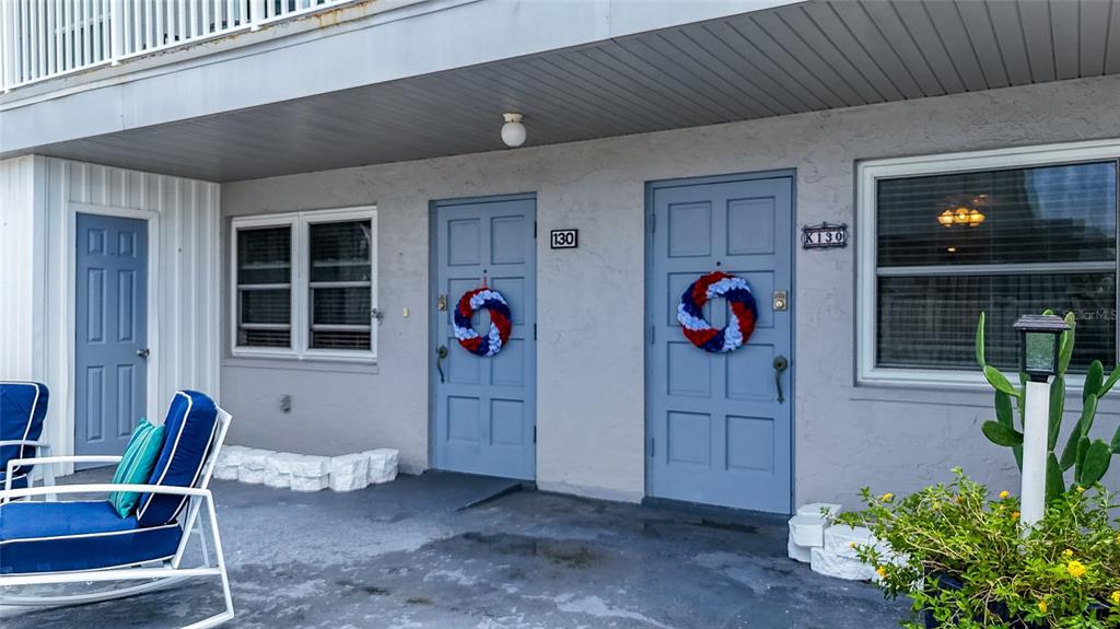A gray building exterior features two blue doors with patriotic wreaths and a patio area — 6777 WINKLER ROAD UNIT 130, FORT MYERS, FL