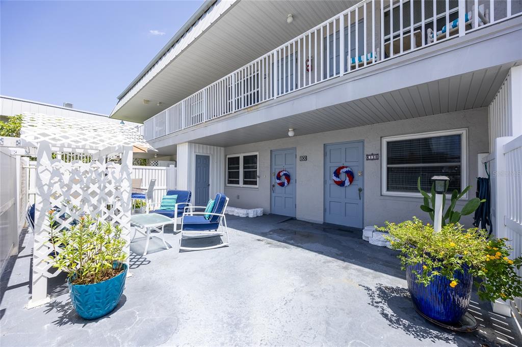 A patio area features two blue doors, outdoor furniture, and potted plants under a balcony — 6777 WINKLER ROAD UNIT 130, FORT MYERS, FL