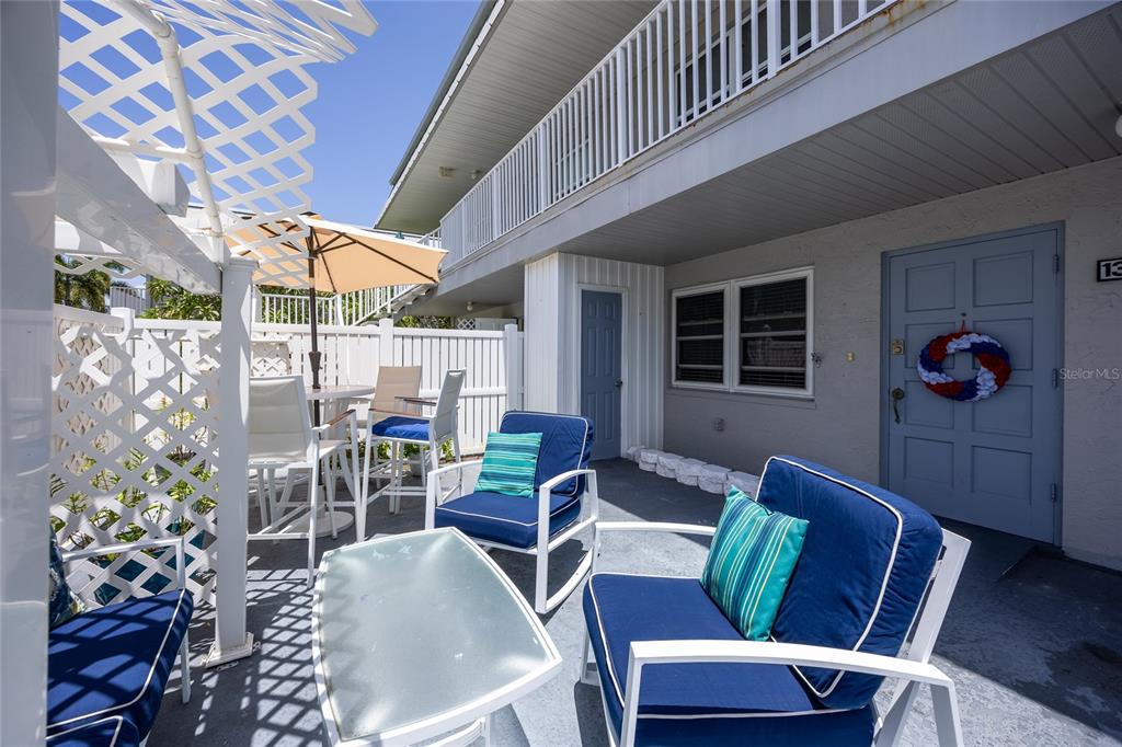 A patio area features outdoor furniture, a glass-topped table, and a blue door with a wreath — 6777 WINKLER ROAD UNIT 130, FORT MYERS, FL
