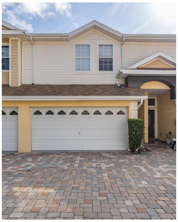 A two-story townhouse exterior features a white garage door, beige siding, and a paver driveway — 2989 ESTANCIA PLACE, CLEARWATER, FL